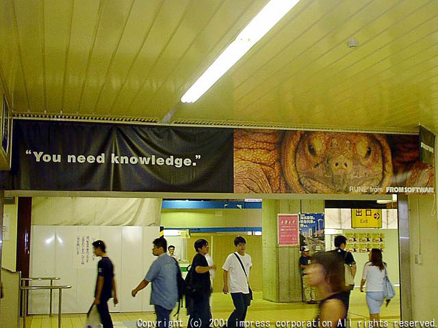 hanging banner of a turtle admist a dark background, hanging from a station ceiling, with a caption saying 'you need knowledge.' and 'RUNE from FROM SOFTWARE' in the bottom right. it appears to be hanging in front of a fluorescent station light, above a station walkway with construction and exit signs and concession in the back. there is a watermark for 'copyright c 2001 impress corporation all rights reserved.'
